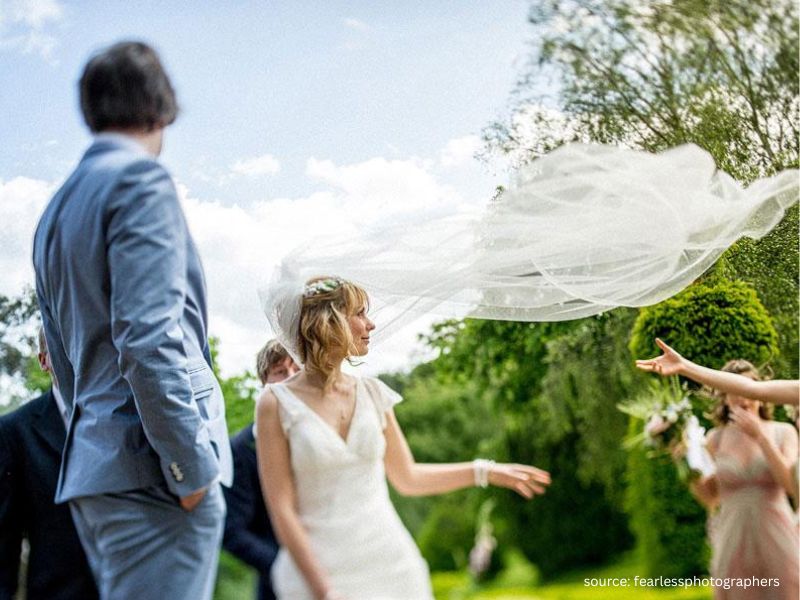 Bride holding veil during windy outdoor wedding ceremony with decor moving in the breeze.