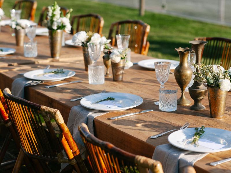 Long rustic farmhouse tables styled for an intimate backyard wedding reception with candles and greenery.