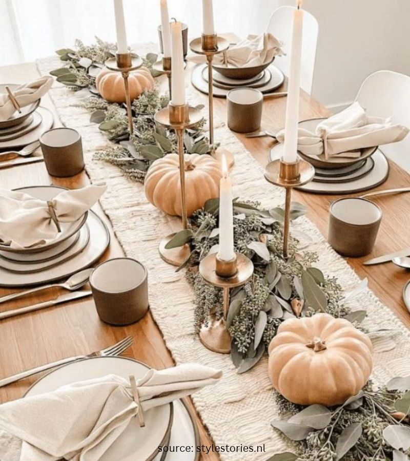 Warm Thanksgiving table with neutral linen, white plates, small pumpkins, greenery, and candles